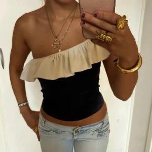 Svart offshoulder topp med volang - Säljer en snygg svart offshoulder topp med bred volang längs halsen. Toppen är axelbandslös och har en tight passform som framhäver midjan. En jättefin fest topp! 