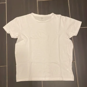 Vit basic t-shirt från 157 - En klassisk vit t-shirt från 157 i 100% bomull. Modellen är enkel med rund halsringning och korta ärmar, perfekt för en clean och stilren look. Passar dig som gillar basic och tidlösa plagg.