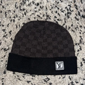 Svart mössa med mönster - Snygg svart mössa med diskret rutigt mönster och vikt kant. Perfekt accessoar för att lyfta din streetstyle. Mjuk och bekväm, passar till de flesta outfits.