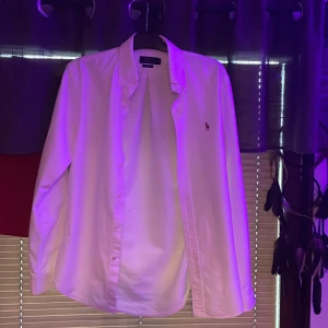 Vit skjorta Polo Ralph Lauren slim fit - Vit långärmad skjorta från Polo Ralph Lauren i slim fit-modell. Klassisk design med knappar framtill och broderad logga på bröstet. Skjortan är tillverkad i bomull och har en stilren look som passar perfekt till jeans eller chinos.