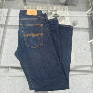 Nudie Jeans Lean Dean – Dry 16 Dips (W30 L30 - Säljer mina Nudie Jeans Lean Dean i tvätten Dry 16 Dips. Riktigt snygg mörk indigo-färg som bara blir bättre med tiden. Modellen är slim fit med lite stretch (99% bomull, 1% elastan) – sitter tajt men bekvämt. Klassiska Nudie-detaljer med oranga sömmar och de välkända bakfickorna. Jeansen är i väldigt fint skick, knappt använda och utan slitningar eller fläckar.  Perfekta till både vardag och fest. Nypris runt 1600 kr – säljes för ett mycket bättre pris 🌿  📏 Storlek: W30 L30 🧵 Modell: Lean Dean 