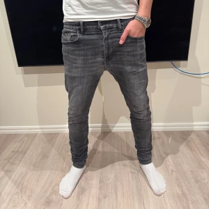 Diesel jeans - Säljer ett par gråa slim fit jeans från Diesel med snygg tvättad look och ett litet hål på låret och röda detaljer vid fickorna. Klassisk femficksmodell med läderpatch bak i midjan och diskret Diesel-logga framtill. Jeansen har smal passform och sitter tajt längs benen.