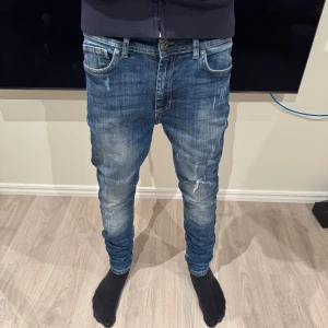 Blå Black Rebel jeans - Snygga blå jeans från Black Rebel med slim passform och slitna detaljer på framsidan. Klassisk femficksmodell, låg midja och lätt tvättad look. Perfekta för dig som gillar en smal siluett och streetstyle. Materialet är stretchigt jeans för extra komfort.