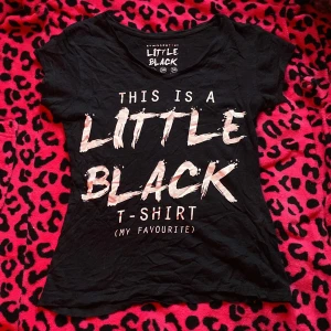 Svart t-shirt från Atmosphere - Svart t-shirt från Atmosphere med trycket 'This is a Little Black T-shirt (my favourite)' i vit text på framsidan. Modellen har korta ärmar och rund hals. Perfekt för dig som gillar statement-plagg och enkel stil.