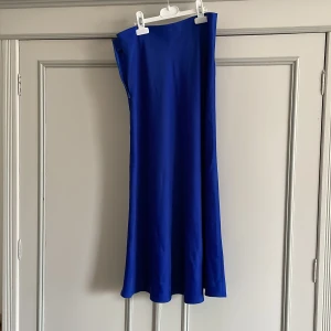 Kornblå långkjol från Selected Femme - En stilren kornblå långkjol från Selected Femme i slät polyesterblandning med dragkedja i sidan. Klänningen har en rak, elegant siluett och är ärmlös, perfekt för dig som gillar minimalistisk och modern stil.