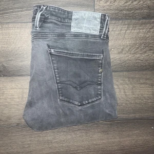 Replay Anbass jeans - Säljer ett par grå Replay jeans med slim fit och klassiska femficksdetaljer. Jeansen har en mörk tvätt, diskreta slitningar och tydliga sömmar på bakfickorna. Perfekta för dig som gillar en tight och modern look. Midja 43cm, längd 102cm. JAG SKICKAR EJ FLER BILDER NÄR JAG BÄR JEANSEN! för storleksguide hänvisar jag till måtten och för bättre inblick i passformen rekommenderar jag att googla på modellnamnet :) s3