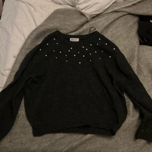 Svart stickad tröja med pärlor H&M - Mysig svart stickad tröja från H&M med pärldetaljer över axlar och bröst. Tröjan har rund halsringning och långa ärmar, perfekt för att lyfta din outfit med lite extra bling.