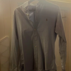 Blå skjorta från Polo Ralph Lauren - Snygg ljusblå skjorta från Polo Ralph Lauren med klassisk button-down krage och broderad logga på bröstet. Skjortan har lång ärm och knappar framtill. Perfekt för dig som gillar stilrena och tidlösa plagg. Passar bäst på någon som är M! PRISET ÄR DISKUTERBART!!!!