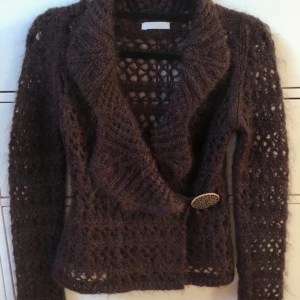 Brun mohair stickad kofta från Promod - Säljer en mohair brun, fluffig och stickad kofta från Prompod med långärmad design och ett snyggt hålmönster. Koftan har en stor dekorativ guldknapp framtill och bred krage som ger en chill vibe. Perfekt att slänga över en t-shirt när det är lite kyligt.