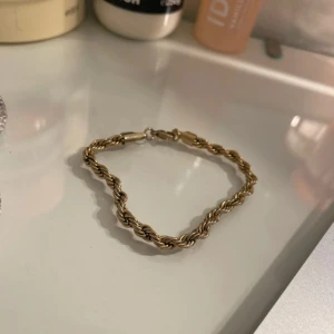 Guldigt tvinnat armband - Snyggt armband i guldig färg med tvinnad kedja och klassiskt lås. Perfekt accessoar för att lyfta din outfit med en trendig och stilren detalj. Passar dig som gillar smycken med lite extra edge.