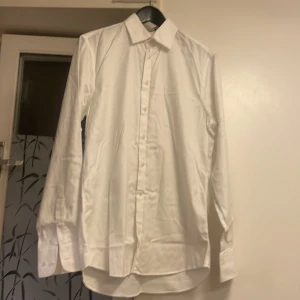 Vit skjorta från Suitsupply Traveller från Italien  - Vit klassisk skjorta från Suitsupply Traveller med lång ärm och knappar framtill. Skjortan har en stilren krage och är tillverkad i mjuk bomull. Perfekt för dig som gillar clean och enkel stil med snygg passform  extra slim fit