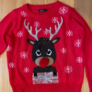 Röd jultröja från KappAhl - Superfin röd stickad jultröja från KappAhl med ett gulligt renmotiv, glittriga horn, snöflingor och en stor röd boll som nos. Tröjan har långa ärmar och ribbade muddar. Perfekt för att maxa julkänslan! Använd relativt få gånger 😊