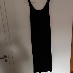 Svart ribbad långklänning H&M Mama S - Svart långklänning från H&M Mama i storlek S. Klänningen är ärmlös med rundad halsringning och har ett ribbat tyg som ger en snygg struktur. Slits nertill på ena sidan för extra rörelsefrihet. Perfekt för dig som vill ha en enkel och stilren look.