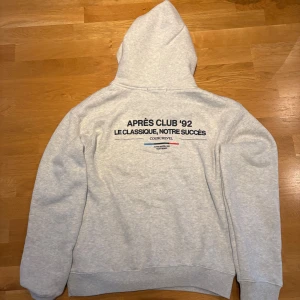 Grå hoodie från Notre Succès - Snygg ljusgrå hoodie från Notre Succès med tryck på ryggen 'APRÈS CLUB '92' tröjan kostar 900 nypris och är helt oanvänd med lapparna kvar, den passar även M då den är liten i stoleken