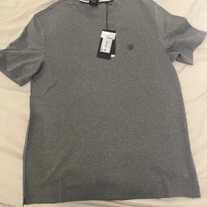 Grå BOSS t-shirt  - Snygg grå t-shirt från BOSS i mjuk bomull. Klassisk rund halsringning och korta ärmar. Diskret BOSS-logga på bröstet och stilren design som passar till allt. Perfekt för dig som gillar enkel och clean stil. Tröjan är köpt i Dubai och är helt ny 10/10 i skick. Storlek S men passar M