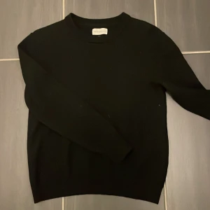 Svart merinoulltröja These Glory Days - En stilren svart tröja från These Glory Days i mjuk merinoull. Klassisk rund halsringning och lång ärm, perfekt för lager på lager. Enkel och clean design som funkar till allt. Superior Merino-kvalitet för extra komfort.