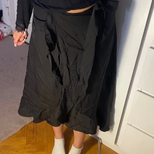 Lång omlott kjol - Elegant svart omlottkjol med knytning i midjan. Lätt, flowy tyg som faller fint – perfekt för både vardag och kväll! Passar storlek S–M  Fint skick ✨  🖤 Enkel att styla med linne, croptop eller skjorta – funkar året runt!