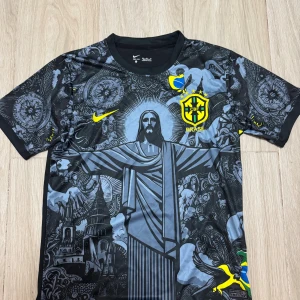 Nike Brasil Dri-Fit fotbollströja M - Unik svart och grå Brasilien fotbollströja från Nike med Dri-Fit-material. Framsidan har ett stort tryck av Kristusstatyn och detaljerade grafiska mönster, samt gula Brasil-loggor och Nike Swoosh. Korta ärmar med tryck och rund hals.