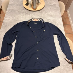 Blå burberry skjorta - Tjena säljer nu min burberry skjorta den är i ny skick använd 1-3 gånger den är i storlek M Passar även S om du inte vill ha lika slimmad passform den kostar runt 5000 ny kontakta om du vill ha bild hur den sitter på är 180 och väger 57 den sitter lite stort på mig så passar nog dig för 180+ och 65 kg + beroende på hur du vill att den ska sitta.    