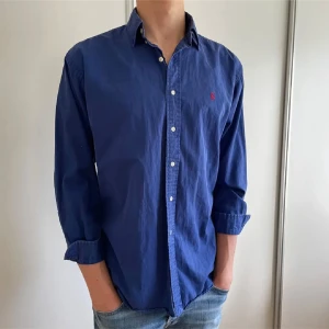 Mörkblå Ralph Lauren skjorta -  mörkblå Ralph Lauren skjorta med klassisk röd broderad logga på bröstet skjortan är i mycket bra skick och har inga fläckar eller skador✅🤩skjortan är väldigt stilren och passar till alla högtider💯 nypris:1200kr mitt pris:449kr priset är självklart inte hugget i sten🪨