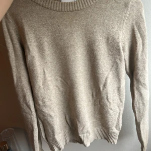 Beige stickad tröja från VILA - Mysig beige stickad tröja från VILA i storlek XS. Tröjan har rund halsringning och ribbade muddar vid hals, ärmslut och nederkant. Perfekt för lager-på-lager och chill dagar. Enkel och stilren design som funkar till jeans eller kjol.