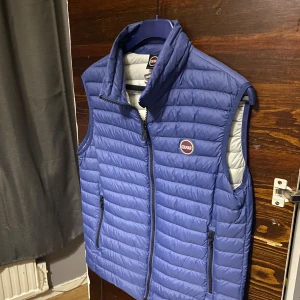 Blå dunväst från Colmar - Snygg blå dunväst från Colmar med quiltad design och dragkedja framtill. Västen har två praktiska fickor med dragkedja och hög krage. Perfekt för lager-på-lager och ger en sportig vibe. Insidan är ljusgrå och västen har Colmar-logga på bröstet.