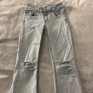 Ljusblå bootcut jeans med slitningar - Snygga ljusblå jeans med bootcut passform och slitna detaljer på knäna. Baksidan har coola fickor med rosa broderat mönster. Ganska stretchiga.