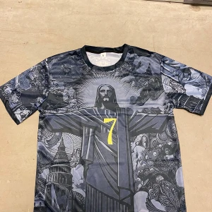 Brasilien Vini Jr. #7 fotbollströja M - Unik Brasilien fotbollströja med Vini Jr. och nummer 7 i gult på ryggen. Framsidan har ett detaljerat grafiskt tryck med Kristusstatyn och coola mönster i mörkblå och grå toner. Korta ärmar och rund hals, tillverkad i lätt polyester som andas.