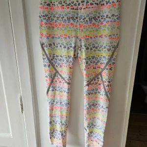 Röhnisch leopardmönstrade leggings - Snygga träningsleggings från Röhnisch med färgglatt leopardmönster i neonrosa, gul, blå och grå på vit botten. De har detaljer i reflex längs benen och logga bak. Stretchigt material som sitter tight och följer kroppen perfekt.