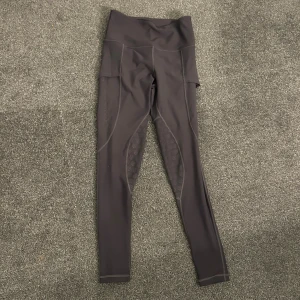 Gråa leggings från Maya Delorez - Snygga gråa leggings från Maya Delorez med hög midja och coola detaljer längs benen. Materialet är stretchigt syntet som sitter skönt och följer kroppen. Perfekta för träning eller ridning, med diskret logga på benet och smarta sömmar.