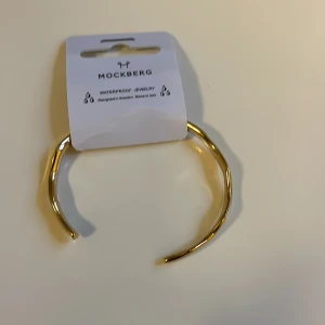 Mockberg armband med en vågformad design från vår Wavy-kollektion.Tillverkat i rostfritt stål med 18K guld PVD-plätering  - Säljer ett snyggt och stilrent vågformad armband från Mockberg Wavy-kollektion. Armbandet är tillverkat i rostfritt stål med 18K guld PVD-plätering som är både slitstarkt och vattentåligt, vilket gör att det behåller sin färg och lyster över tid. Den öppna designen ger en flexibel passform som smidigt anpassar sig efter din handled. Har fått mitt armband i present men är för litet för mig.
