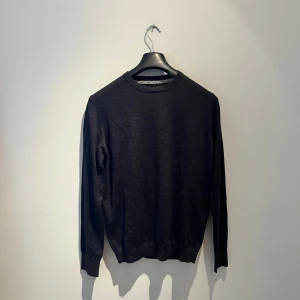 Mörkgrå/svart stickad tröja Bruun & Stengade - En stilren mörkgrå/svart stickad tröja från Bruun & Stengade i storlek M. Tröjan har rund halsringning och långa ärmar med ribbade muddar. Perfekt för dig som gillar enkel och klassisk design med en snygg passform. Hör av er vid frågor 