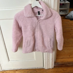 Ljusrosa teddyjacka från Firefly - Supermjuk teddyjacka i ljusrosa från Firefly. Jackan har dragkedja framtill, två fickor och en klassisk krage. Perfekt för dig som gillar en cozy och trendig look. Fodrad insida för extra komfort.