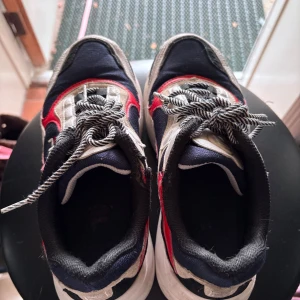 Fila sneakers i rött, vitt och blått - Säljer ett par chunky Fila sneakers med cool retrostil. Skorna har en mix av marinblått, vitt och rött med svartvita snören och Fila-logga på sidan. Ovandelen är i textil och syntet, sulan är vit och rejäl för extra streetkänsla. Perfekta för dig som gillar sportig vibe.