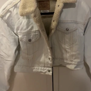 Vit sherpa-jeansjacka från Levi's - Säljer en vit croppad jeansjacka från Levi's med mysigt teddyfoder och krage i sherpa. Jackan har två bröstfickor med knappar och klassiska sömmar. Perfekt för dig som vill ha en cool och varm look under höst och vinter.