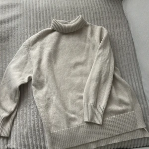 Beige stickad polotröja med slits i sidorna - Beige stickad polotröja med bred ribbad krage och nederkant. Tröjan har slitsar i sidorna som ger en snygg och avslappnad look. Perfekt för lager-på-lager och passar till allt. Mjuk och skön att bära. Size S men då den är oversized passar den i princip alla storlekar