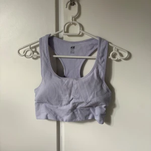 Ljuslila ribbad sporttopp H&M - Säljer en ljuslila ribbad sporttopp från H&M Sport. Toppen är ärmlös med brottarrygg och har en tight passform som sitter skönt vid träning. Tillverkad i stretchig polyesterblandning för extra komfort.