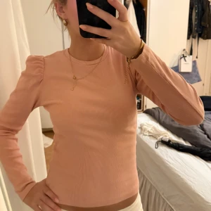 Ljusrosa puffärmad tröja från Pieces - Supersöt ljusrosa ribbad tröja från Pieces med puffade axlar och rund hals. Långärmad och figurnära passform som ger en snygg siluett. Perfekt att styla med jeans eller kjol för en trendig look.