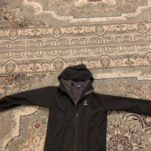 Svart vindjacka från Haglöfs, M - Svart vindjacka från Haglöfs i storlek M. Jackan har huva, hel dragkedja framtill och två sidofickor. Tillverkad i lätt och slitstark polyester, perfekt för blåsiga dagar. Köpt för cirka 1200 behövs ej mer så säljer lågt pris. Som ny inga fläckar.