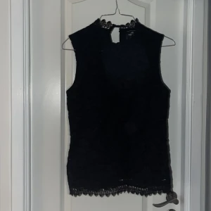 Svart spetsblus från Park Lane - Supersnygg svart blus från Park Lane i spets med hög hals och fina spetsdetaljer både vid halsringningen och nederkanten. Ärmlös modell som ger en elegant och trendig look. Perfekt att styla med jeans eller kjol för en cool outfit.