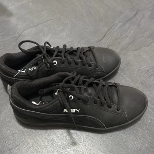 Svarta sneakers från Puma - Svarta sneakers från Puma med klassisk design och vit logga på sidan. Skorna har snörning, rund tå och är tillverkade i syntetmaterial med en platt sula. Perfekta för dig som gillar en clean och stilren look.