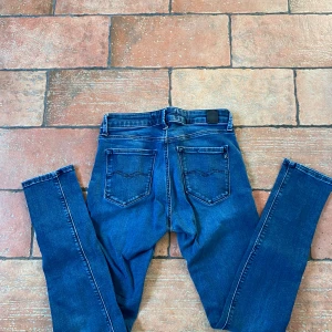 Replay Anbass jeans blå - Säljer ett par Replay Anbass jeans i klassisk blå tvätt. Jeansen har bra passform, fickor och snygga detaljer på bakfickorna. Materialet är stretchigt jeans och de har en modern look med normal midja. Perfekta för dig som gillar en grish fitt.