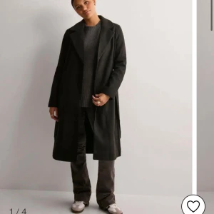 Svart kappa med bälte och fickor - Stilren svart kappa med klassisk krage och bälte i midjan. Lång modell med raka ärmar och två snedställda fickor framtill. Perfekt för dig som gillar minimalistisk look och vill ha en tidlös jacka till garderoben.💕