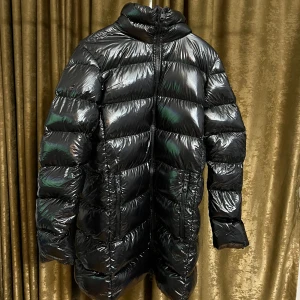 Svart lång dunjacka från RefrigiWear - Säljer en svart, glansig och lång dunjacka från RefrigiWear. Jackan har hög krage, två dragkedjefickor framtill och quiltad design. Fylld med äkta dun för extra värme och har en snygg oversized look. Perfekt för kalla dagar när du vill hålla stilen. Pris kan diskuteras vid snabb affär!🙂