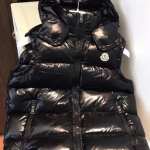 Svart dunväst från Moncler med huva - Snygg svart dunväst från Moncler med glansig finish och huva. Västen har dragkedja framtill, två fickor med dragkedja och klassisk Moncler-logga på bröstet. Perfekt för lager-på-lager och ger en cool streetstyle-vibe.