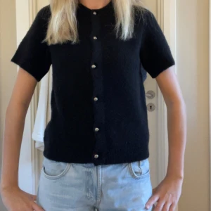 Svart stickad kofta med pärlknappar - Svart stickad kofta med korta ärmar. Perfekt nu till hösten