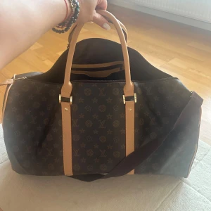 (Vet ej om det ej orginal)Louis Vuitton monogram resväska - (Vet ej om det ej orginal fick som present)Ser utt som Louis Vuitton monogram resväskaStilren och rymlig resväska  i klassiskt monogrammönster. Väskan är brun med ljusbruna handtag och detaljer, har dragkedja och en innerficka med dragkedja. Perfekt för weekendresor och har både handtag och axelrem.