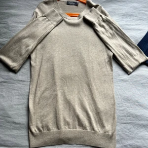 Beige stickad tröja från Dressmann - Snygg beige stickad tröja från Dressmann med rund hals och korta ärmar. Perfekt för dig som gillar enkel och stilren design. Mjuk och skön kvalitet som passar till jeans eller chinos. Enkel att matcha med andra plagg.