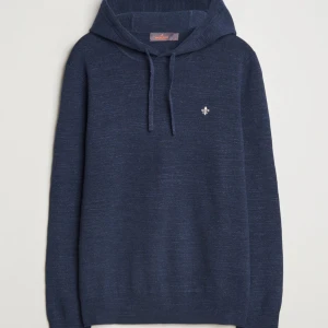 Mörkblå stickad hoodie från Morris - Mörkblå stickad hoodie från Morris med huva och snörning. Tröjan har en liten broderad logga på bröstet och är långärmad. Perfekt för dig som gillar en stilren och bekväm look.