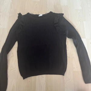 Svart stickad tröja med volang XS - Svart stickad tröja från & Other Stories i storlek XS. Tröjan har lång ärm och snygga volangdetaljer på axlarna. Perfekt för dig som gillar en klassisk look med en twist. Mjuk och skön att bära.